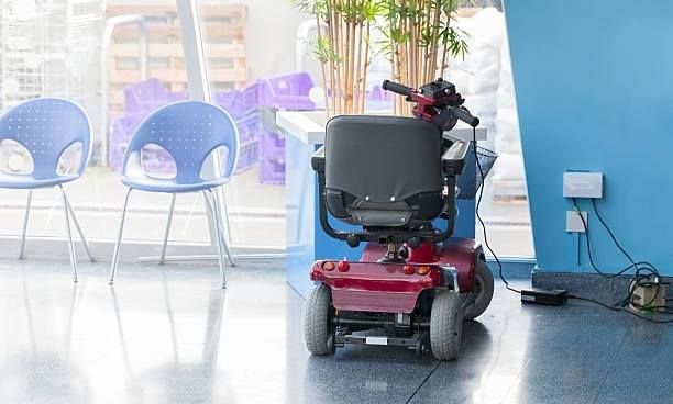 Red motorized wheelchair parked by a blue wall and chairs in a waiting area.