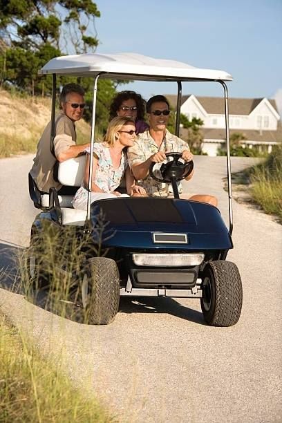 Four people in a blue golf cart, driving on a paved road, sunny day.