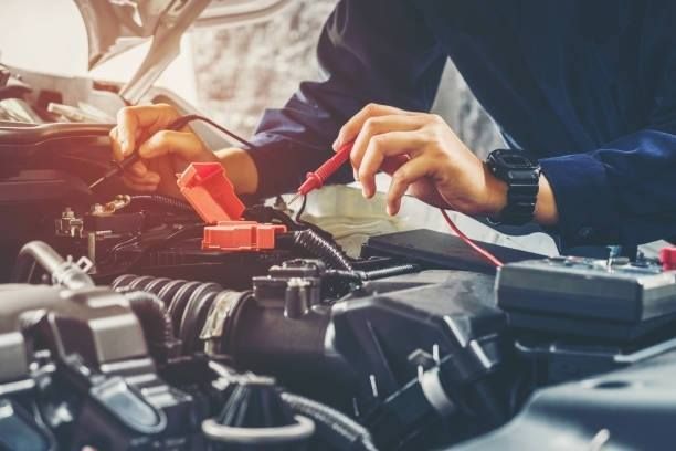 Mechanic using multimeter to test car engine wires, outdoors, close-up.