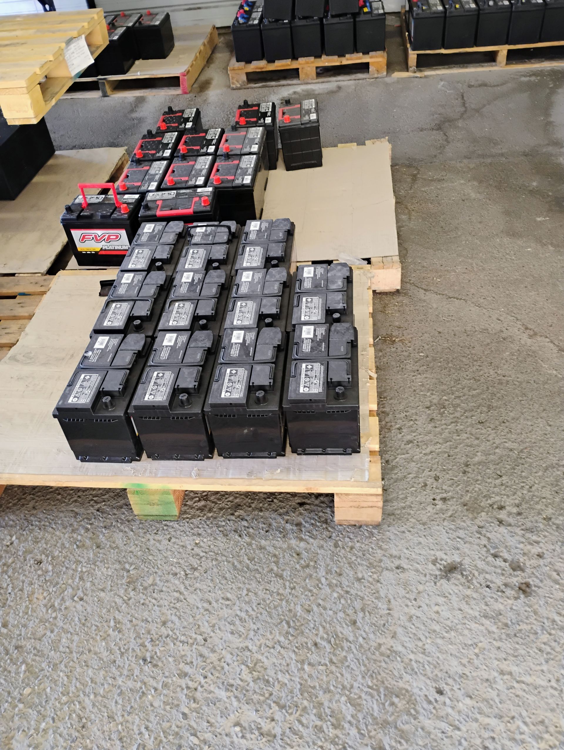 Several car batteries stacked on wooden pallets in a warehouse setting.