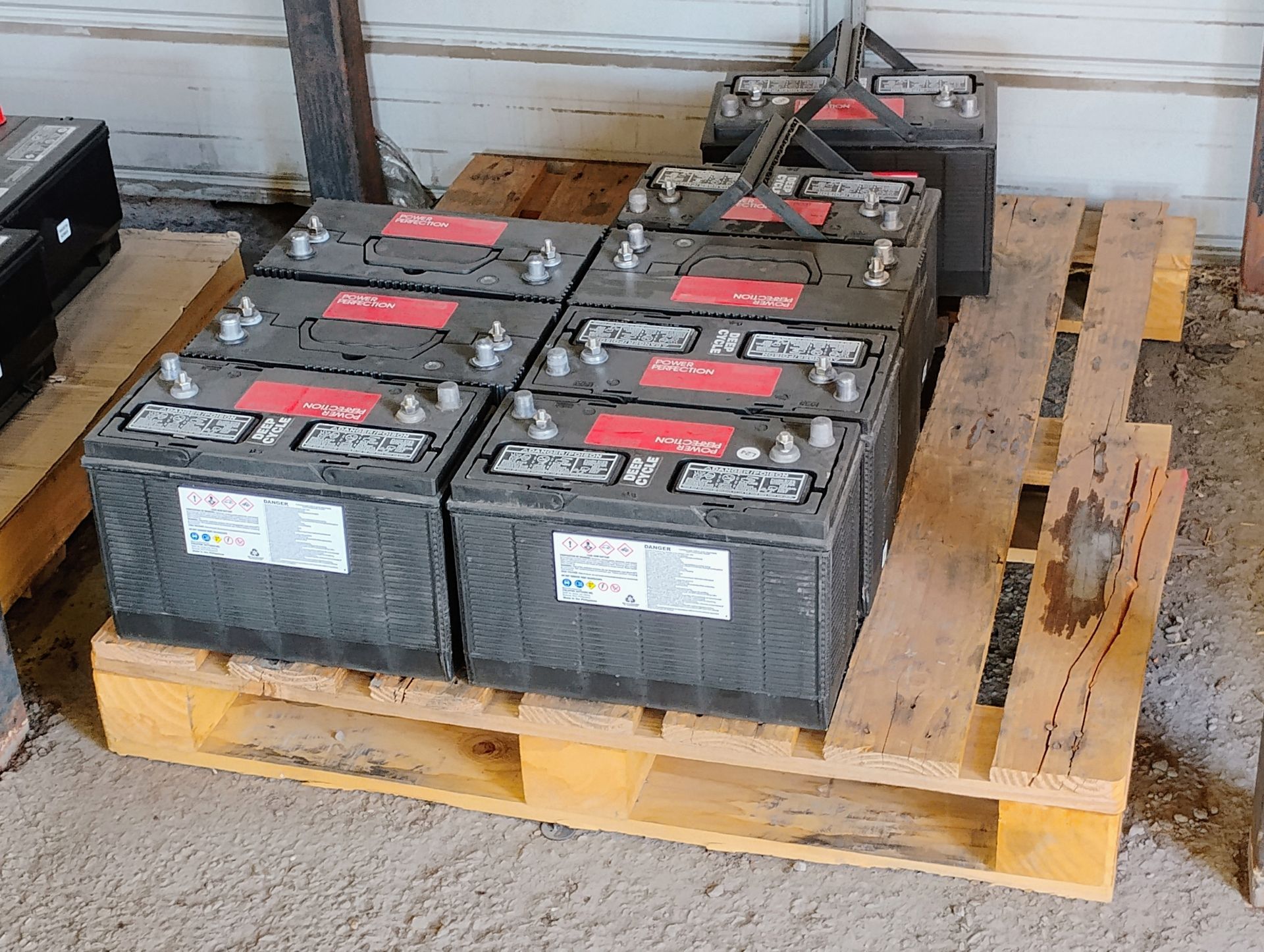 Batteries on a wooden pallet inside a building. The batteries are black with red tops.