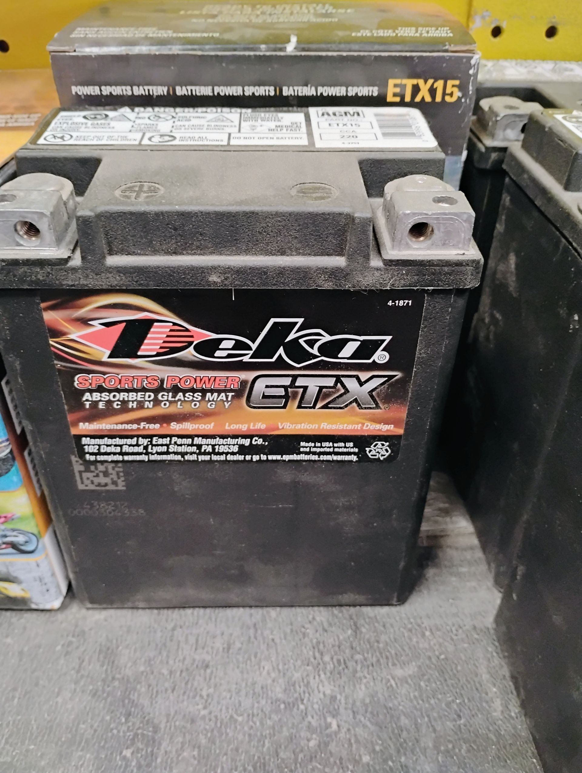 Teko ETX motorcycle battery in a store, black with red and gold label.