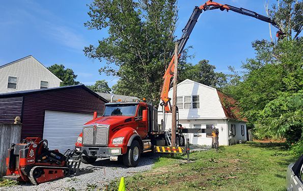 Red truck with crane lifting materials beside a house and garage in a sunny yard
