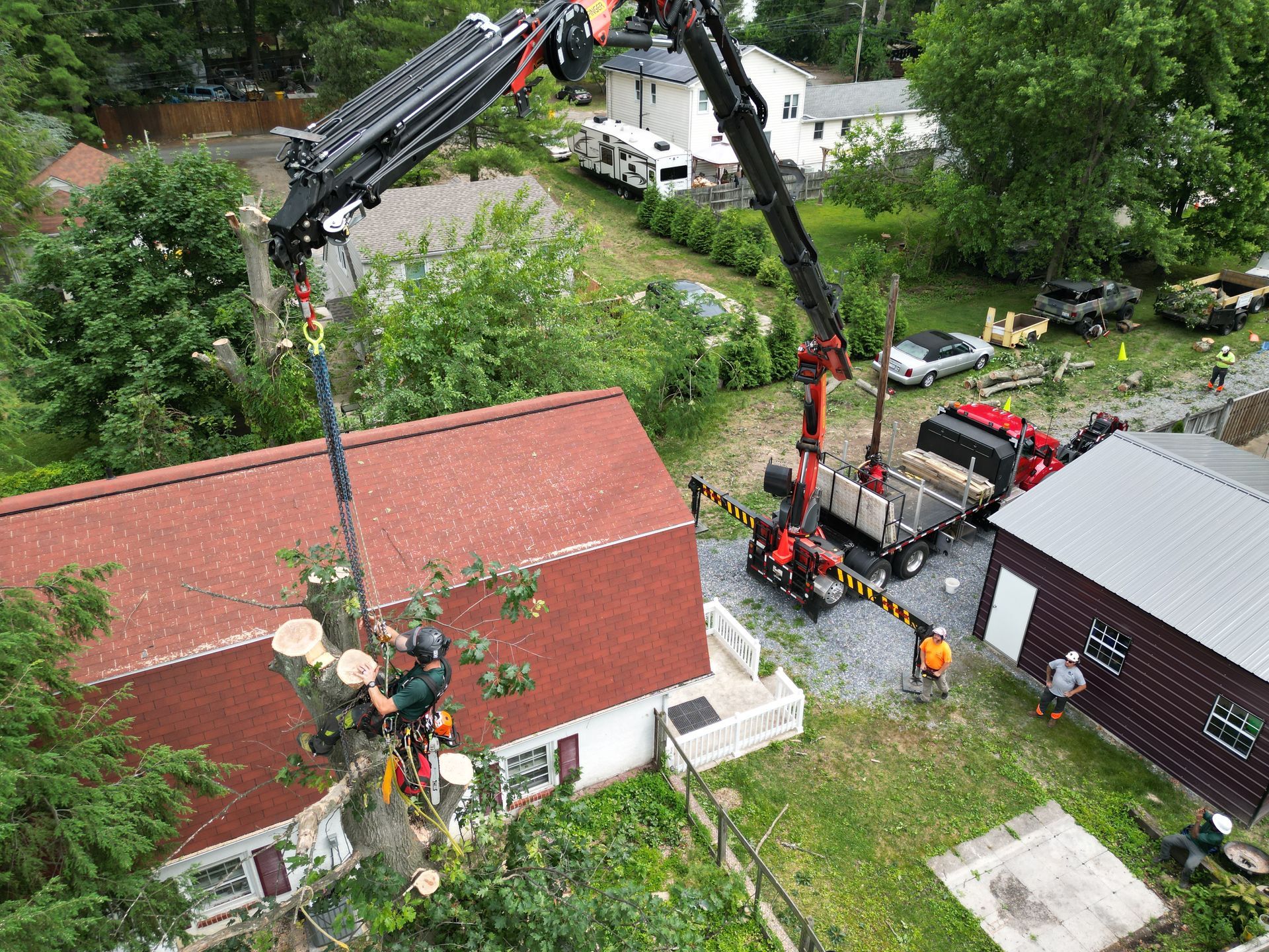 Two cranes lifting a red-roofed structure beside a house and trees.
