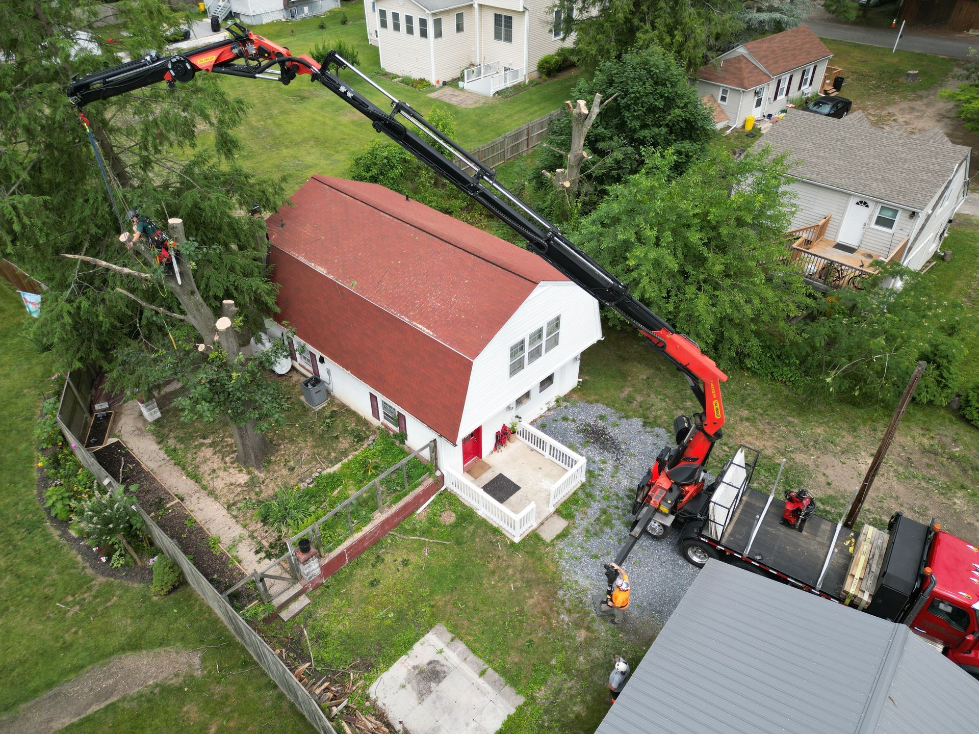 Aerial view of a crane lifting materials over a red-roofed house in a green residential yard.