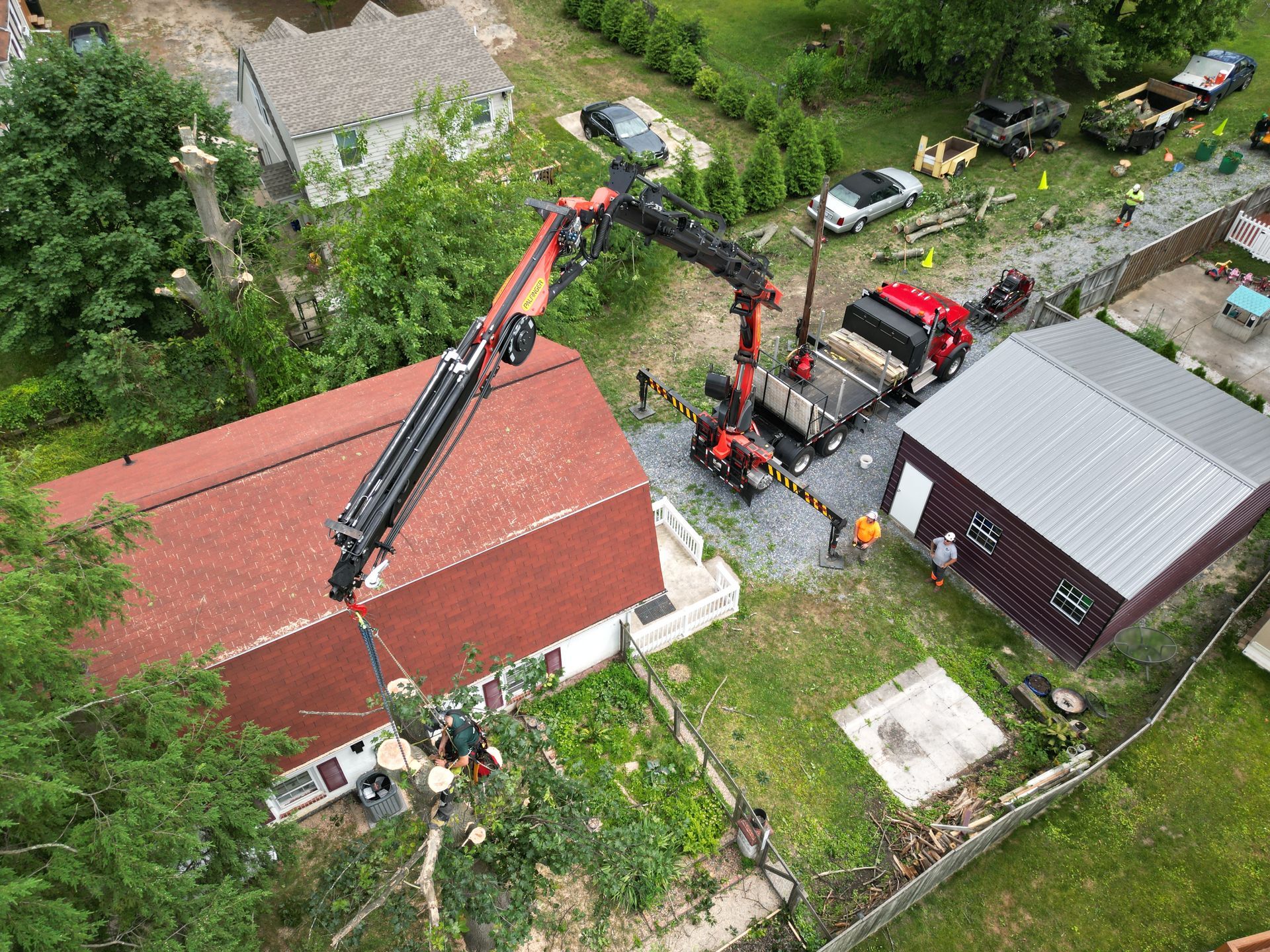 Aerial view of cranes removing a roof on a red building beside a gray building and parked trucks.