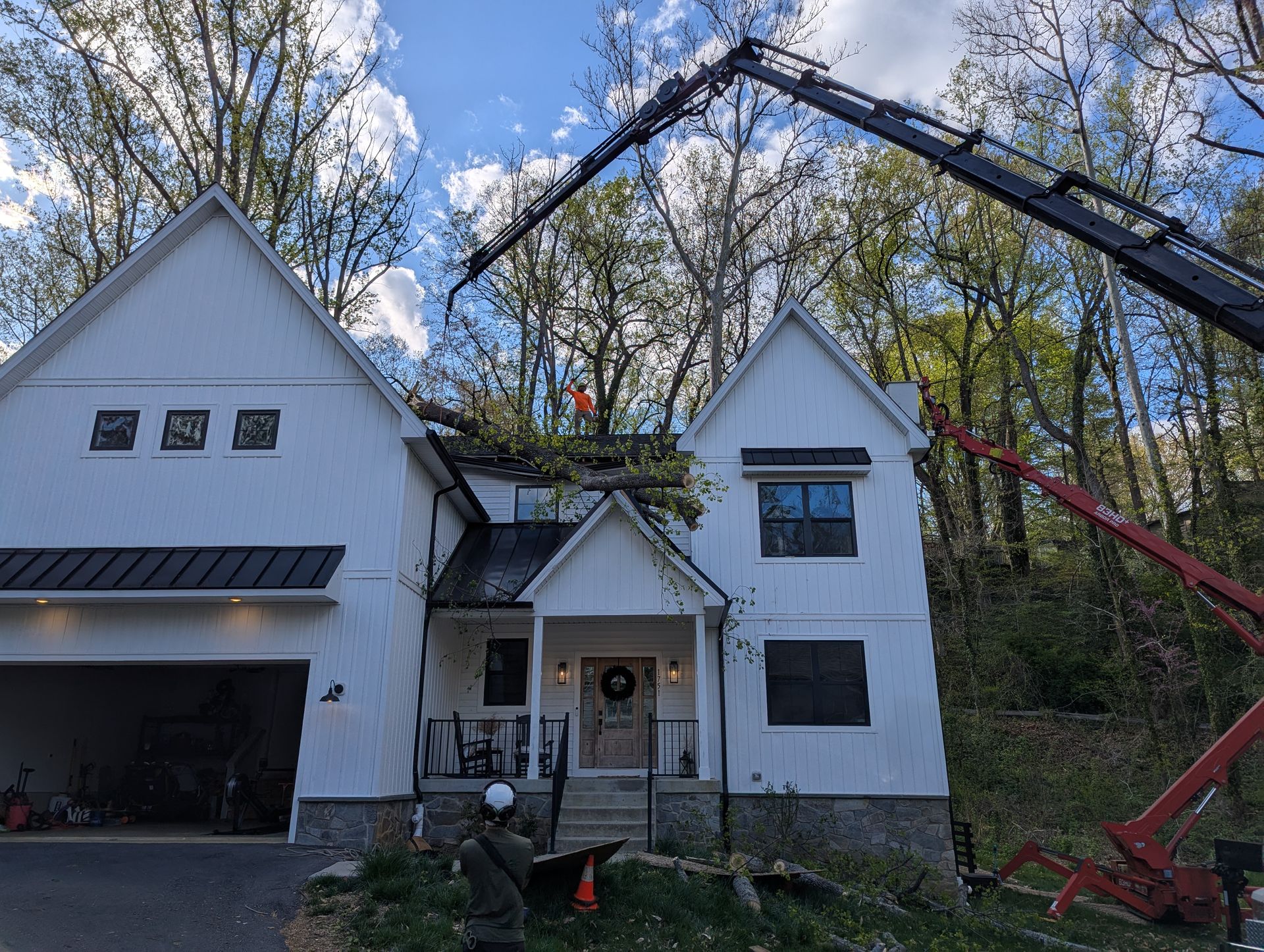 Two-story white house with a raised crane basket near the roof in a wooded yard
