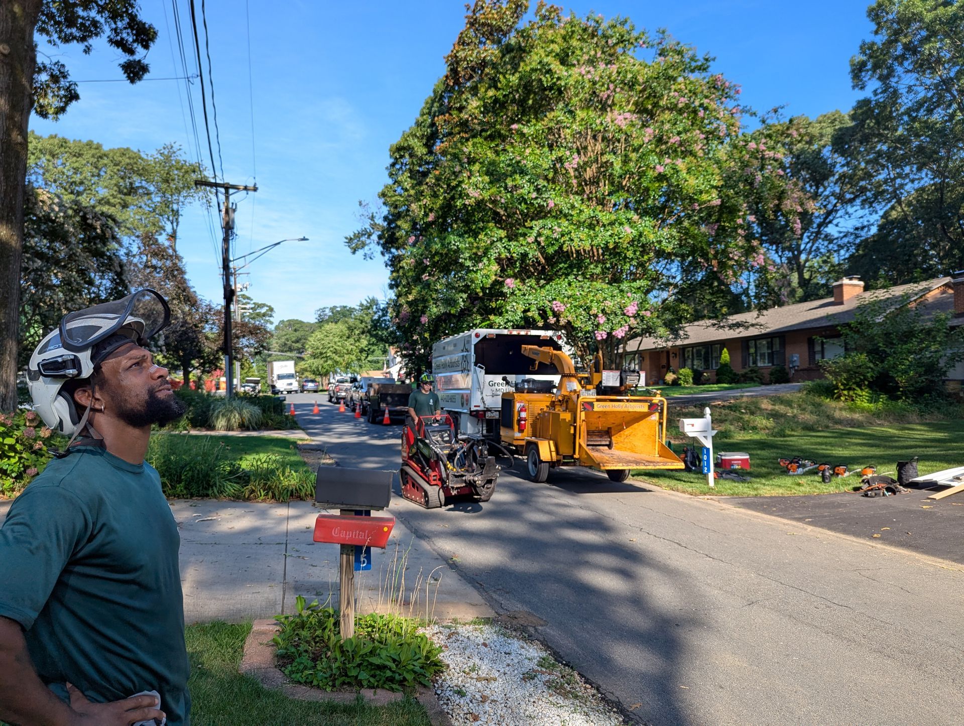 Street scene with a worker near a yellow wood chipper and truck on a residential road under blue sky