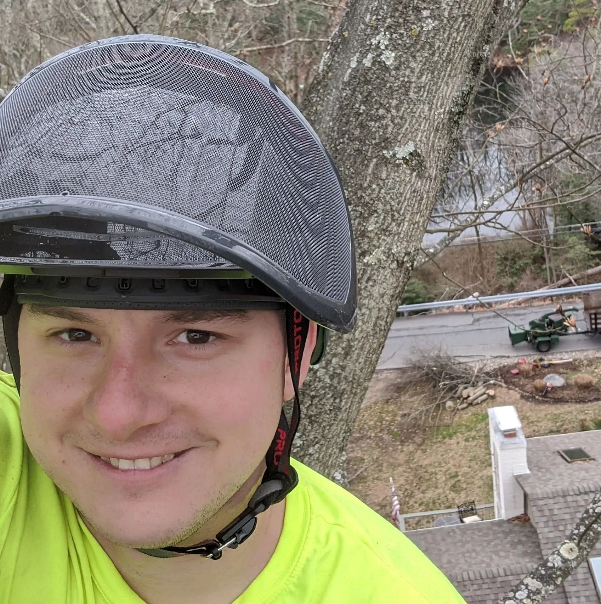 Smiling cyclist wearing a gray helmet and neon yellow jacket outdoors by a tree and stairs