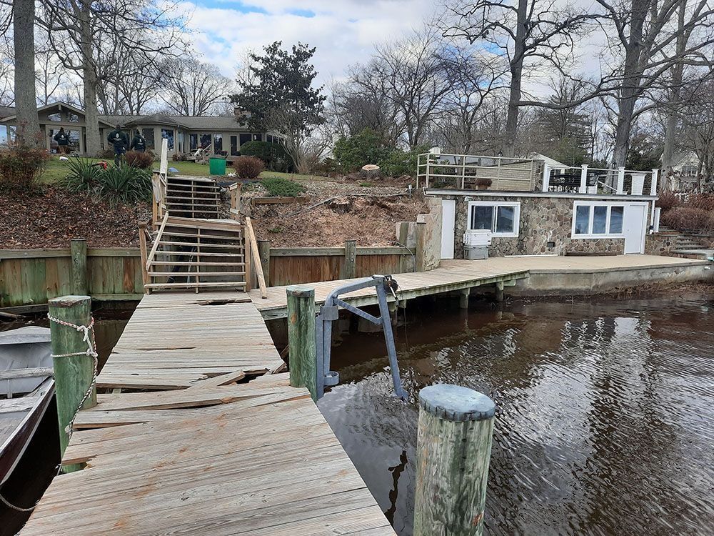 Wooden dock leading to a lakeside cottage with stairs, trees, and calm water on a cloudy day