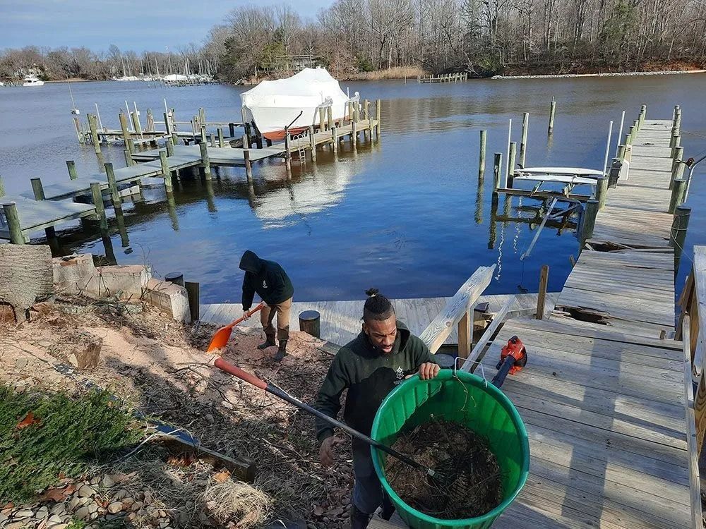 People with buckets and tools working by a dock beside a calm river