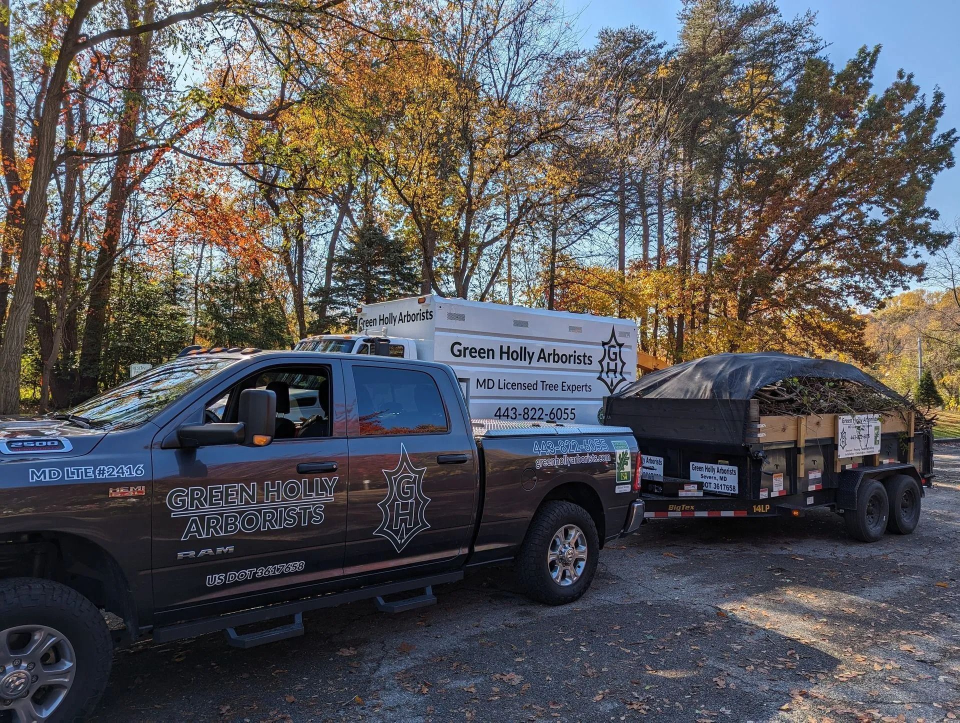 Black pickup truck towing a trailer with kayaks and equipment on a gravel road in autumn woods