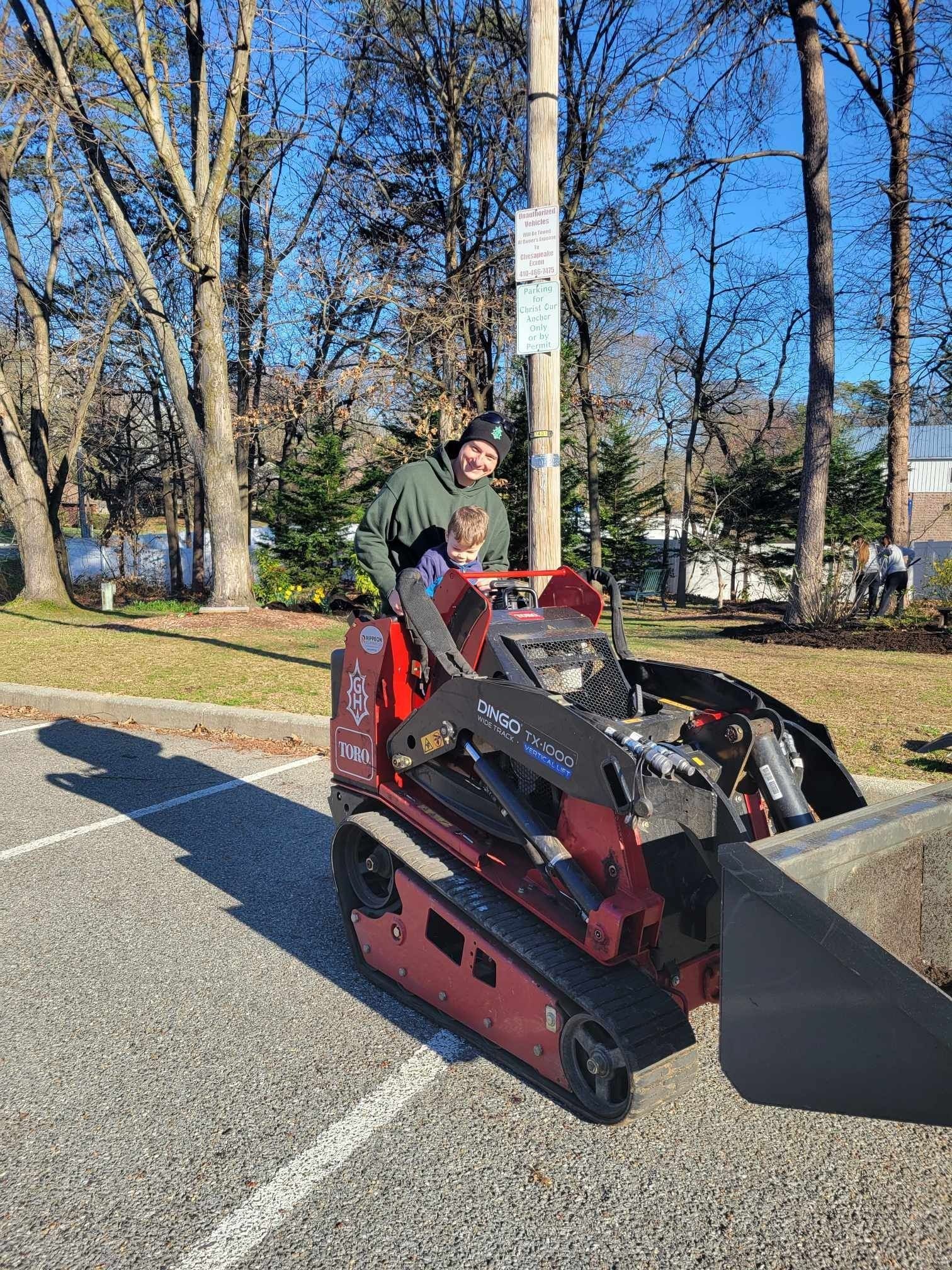 Person on a red skid-steer loader clearing a paved path on a sunny day