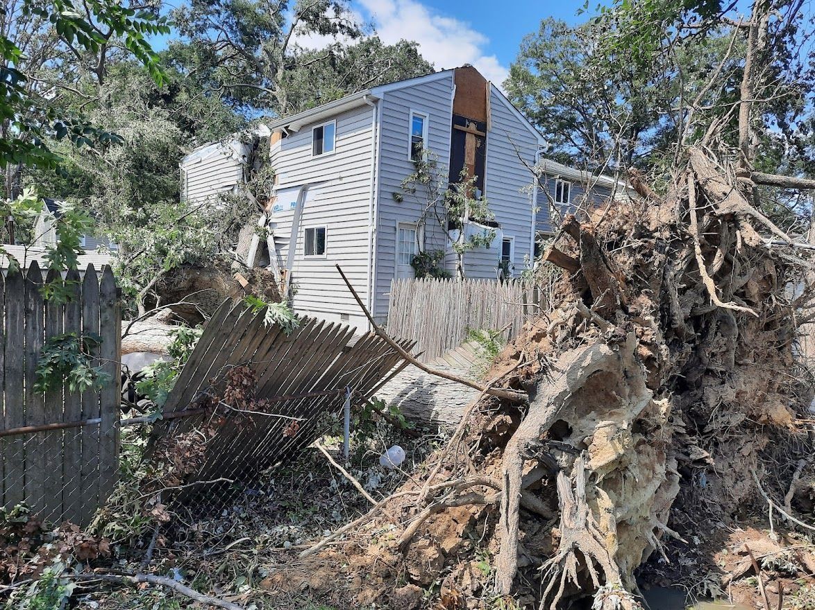 Damaged white house with fallen tree debris in the yard after a storm