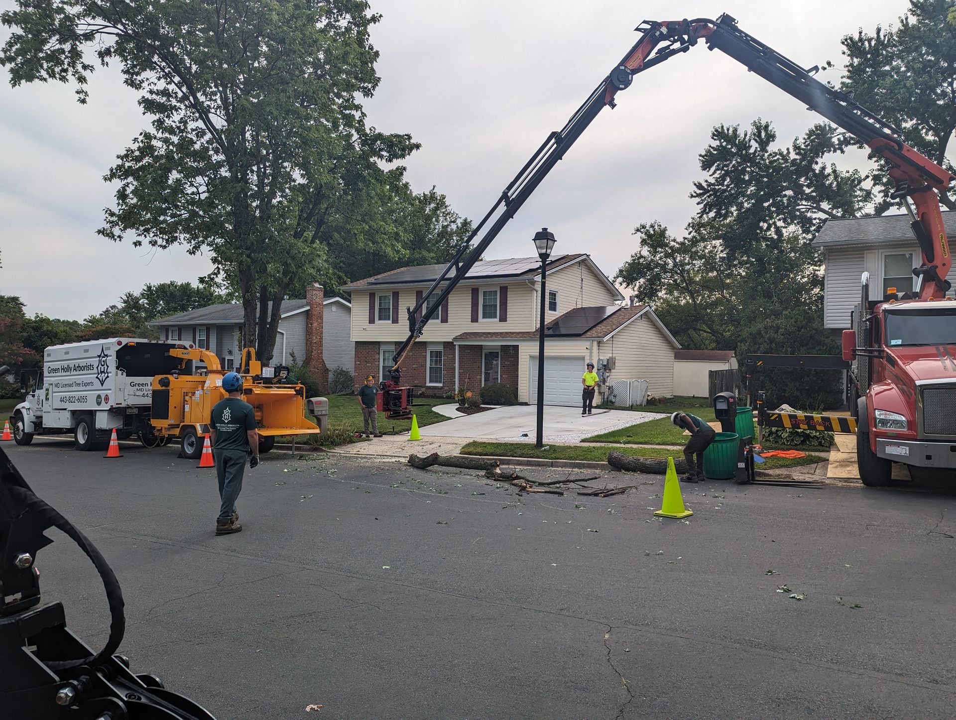 Construction crew using a crane to clear debris in front of a damaged house on a residential street