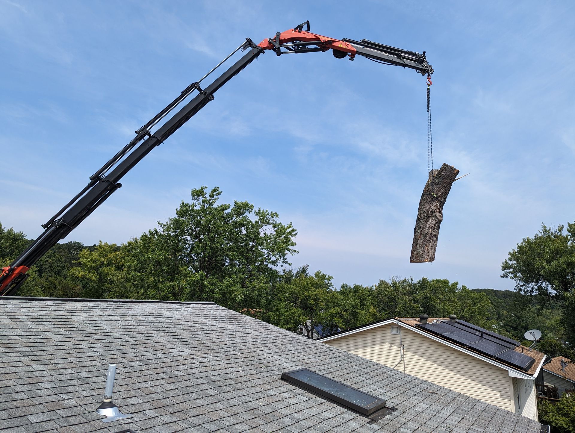 Crane lifting shingles off a house roof under a blue sky