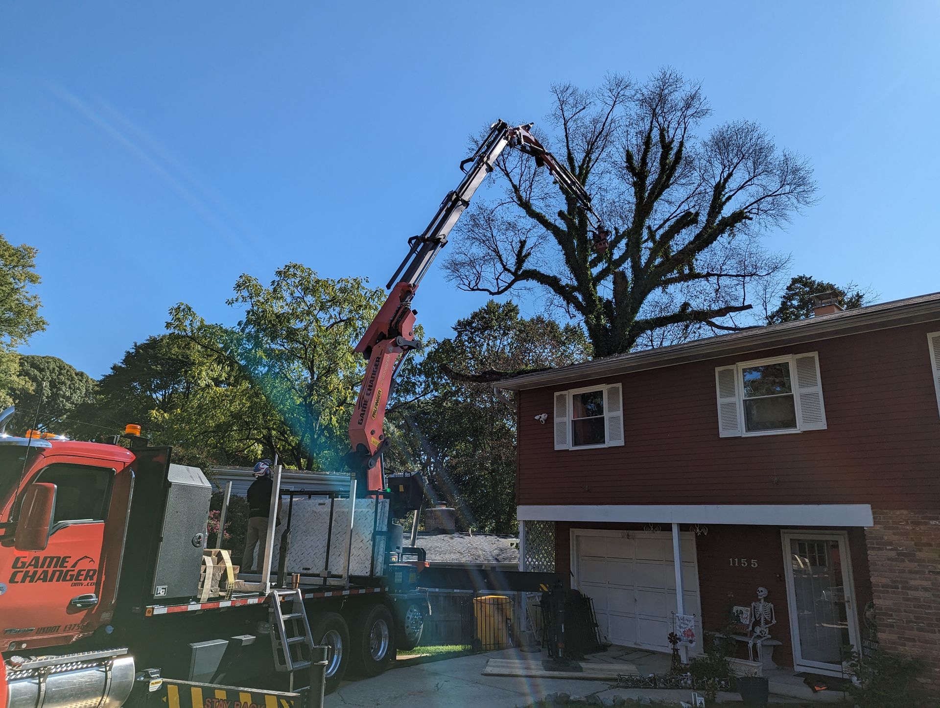 Crane trimming a large tree beside a two-story house on a sunny day