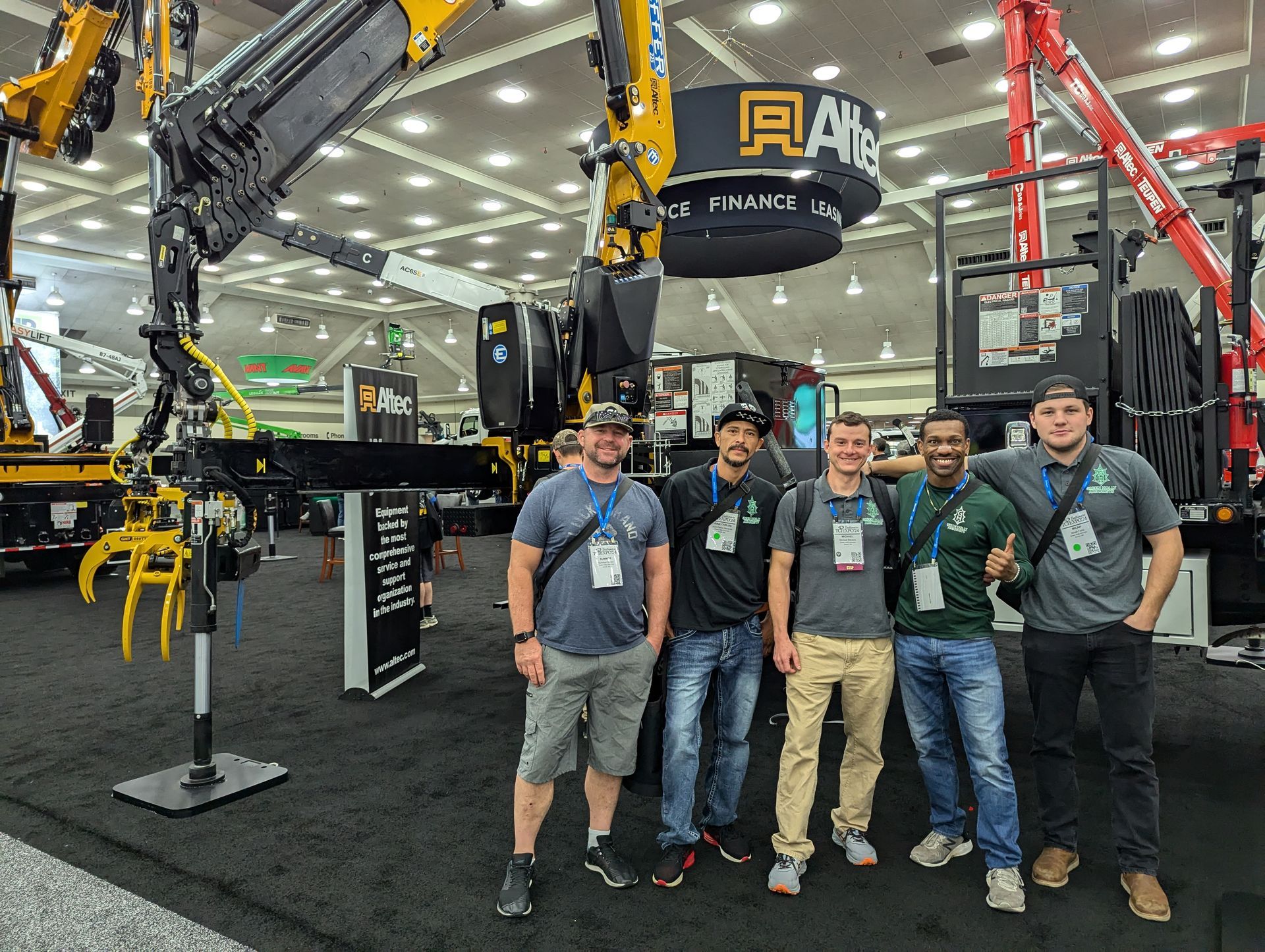 Four people posing at a trade show booth beside large yellow industrial equipment and machinery.