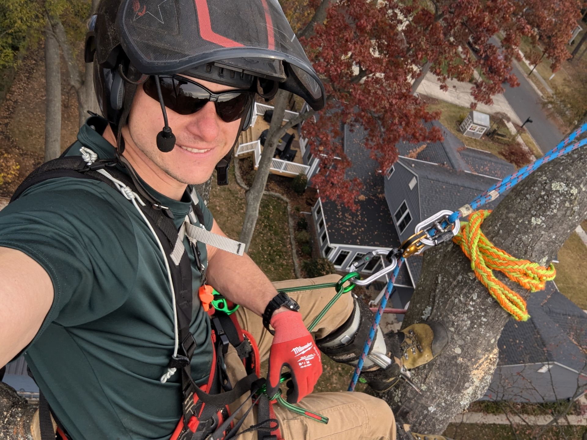 Climber selfie on a rope beside a rocky cliff, wearing a helmet, sunglasses, and red gloves.