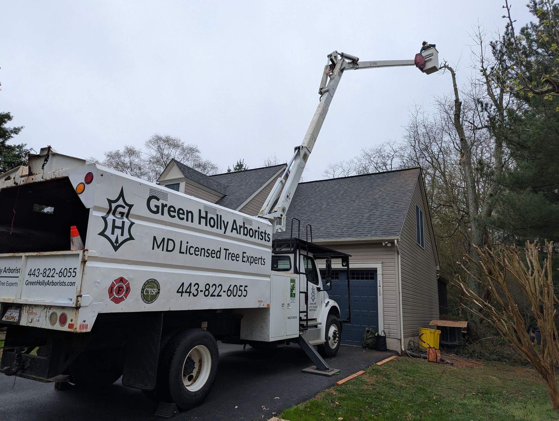 Green Holly Homes work truck with boom lift extended toward a house in a driveway