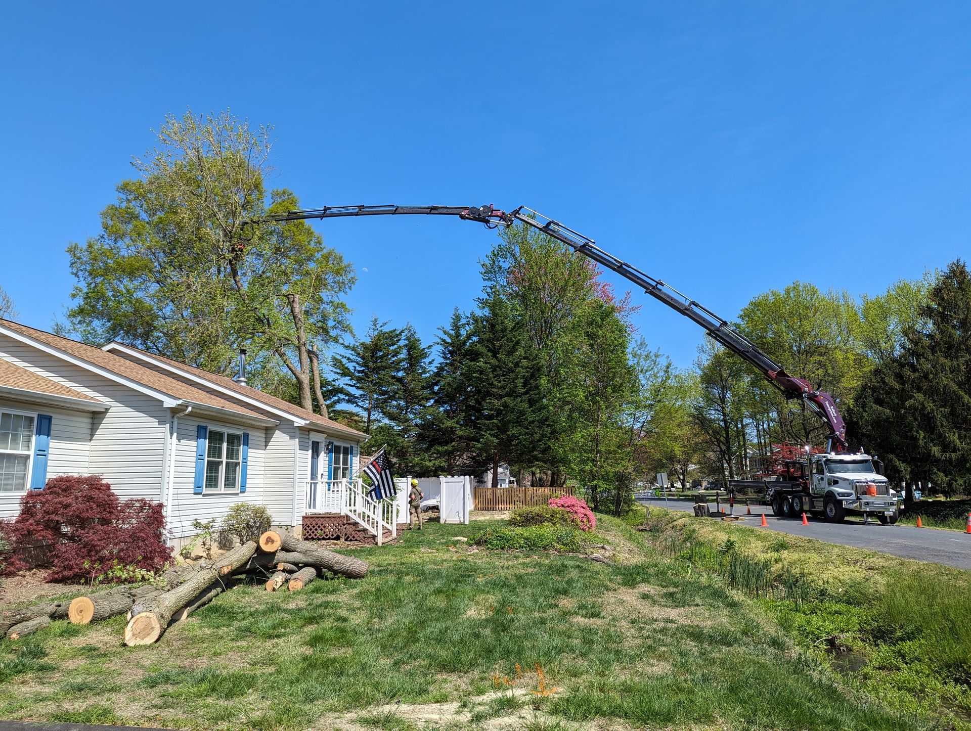 Tree-trimming truck with boom extended over a house and driveway on a sunny suburban street