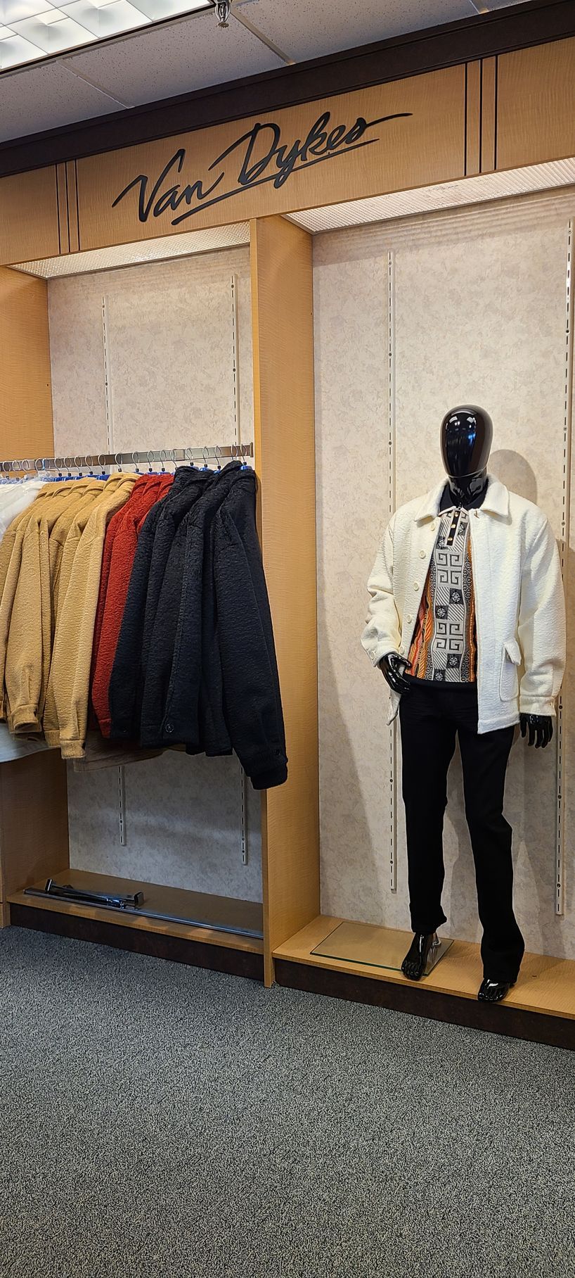 Clothing display with hanging jackets and a mannequin in a white jacket and black pants inside a store.