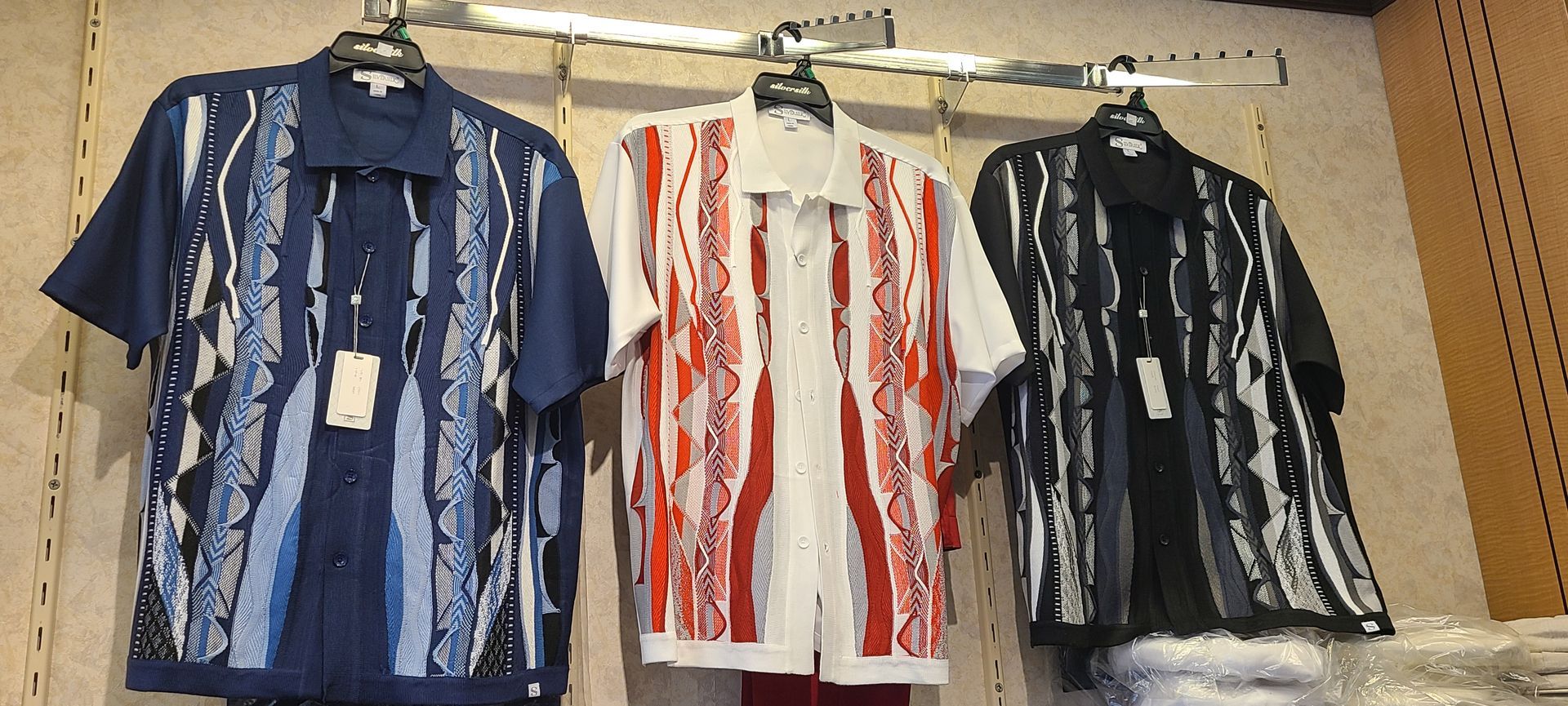 Three patterned button-up shirts hanging on hangers in a cardboard box