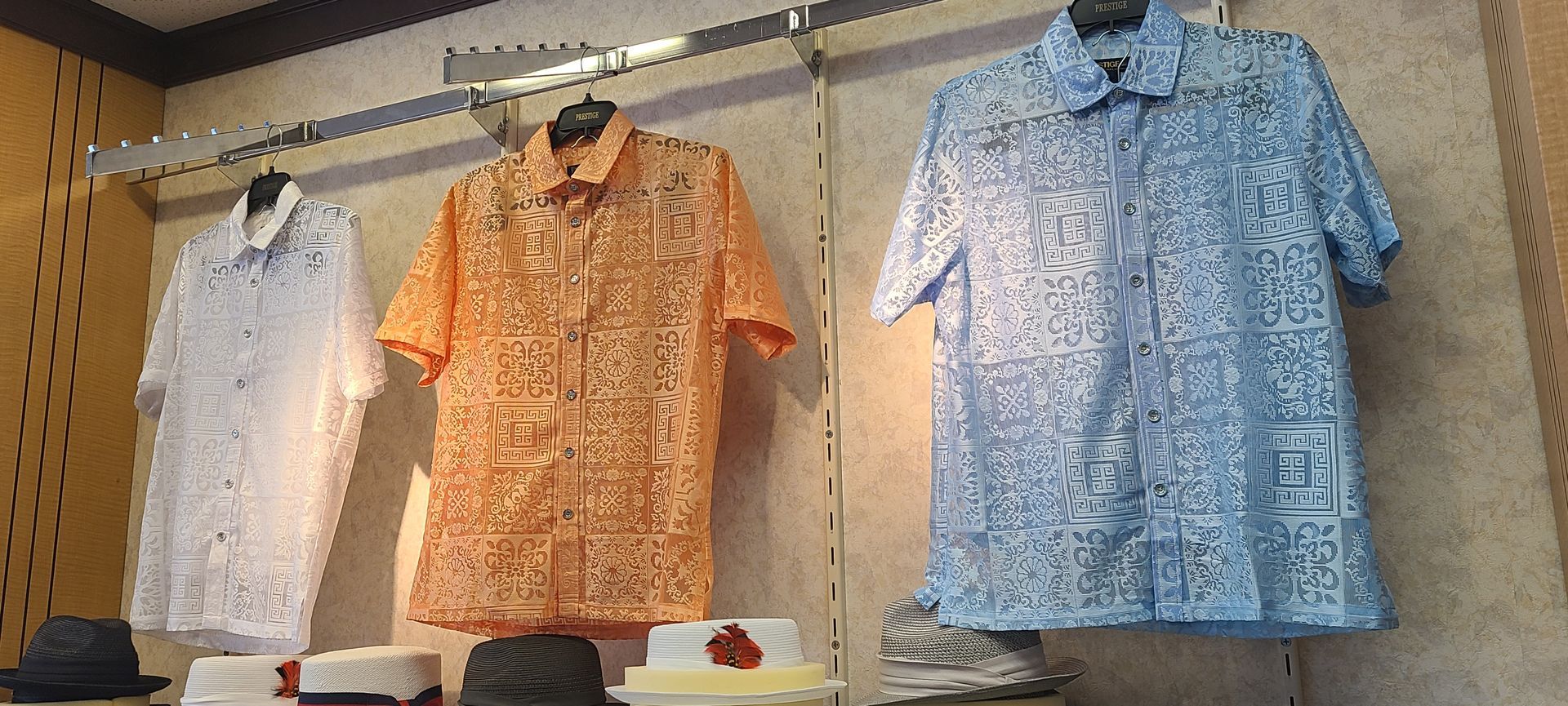 Three patterned short-sleeve button-up shirts in white, orange, and blue hanging on a store rack