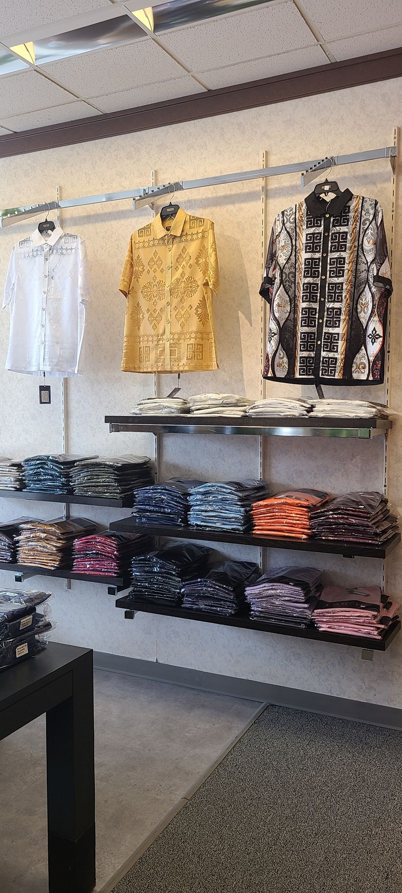 Clothing store display with patterned shirts hanging above folded stacks of jeans and pants on shelves