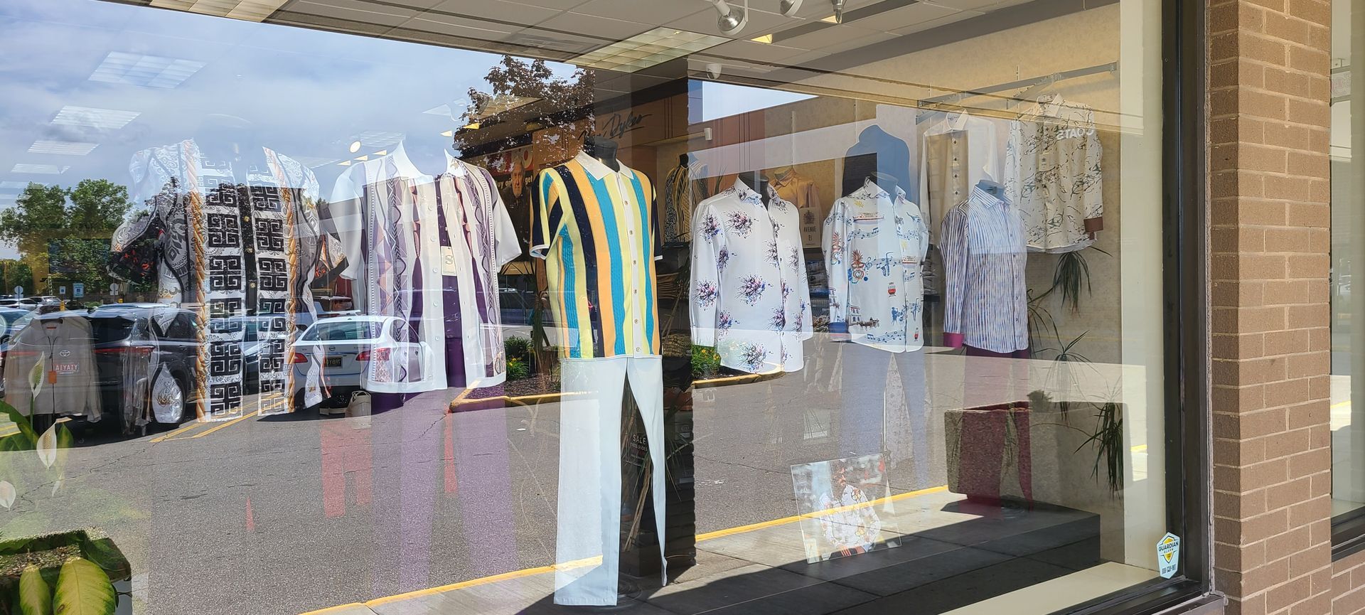 Clothing store window display with hanging shirts, a striped top, and pants reflected in the glass