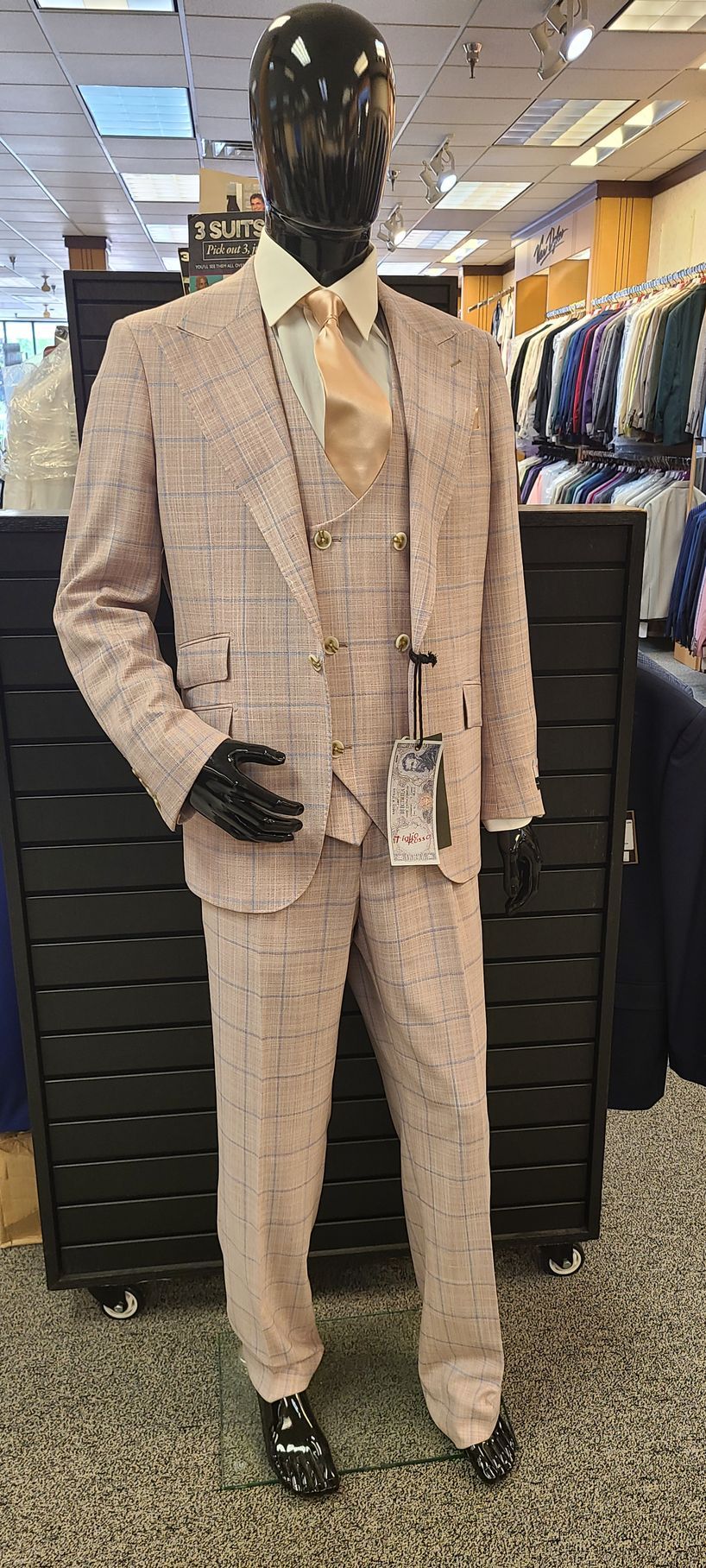 Mannequin in a beige plaid suit, tan vest, and tie standing in a clothing store display.