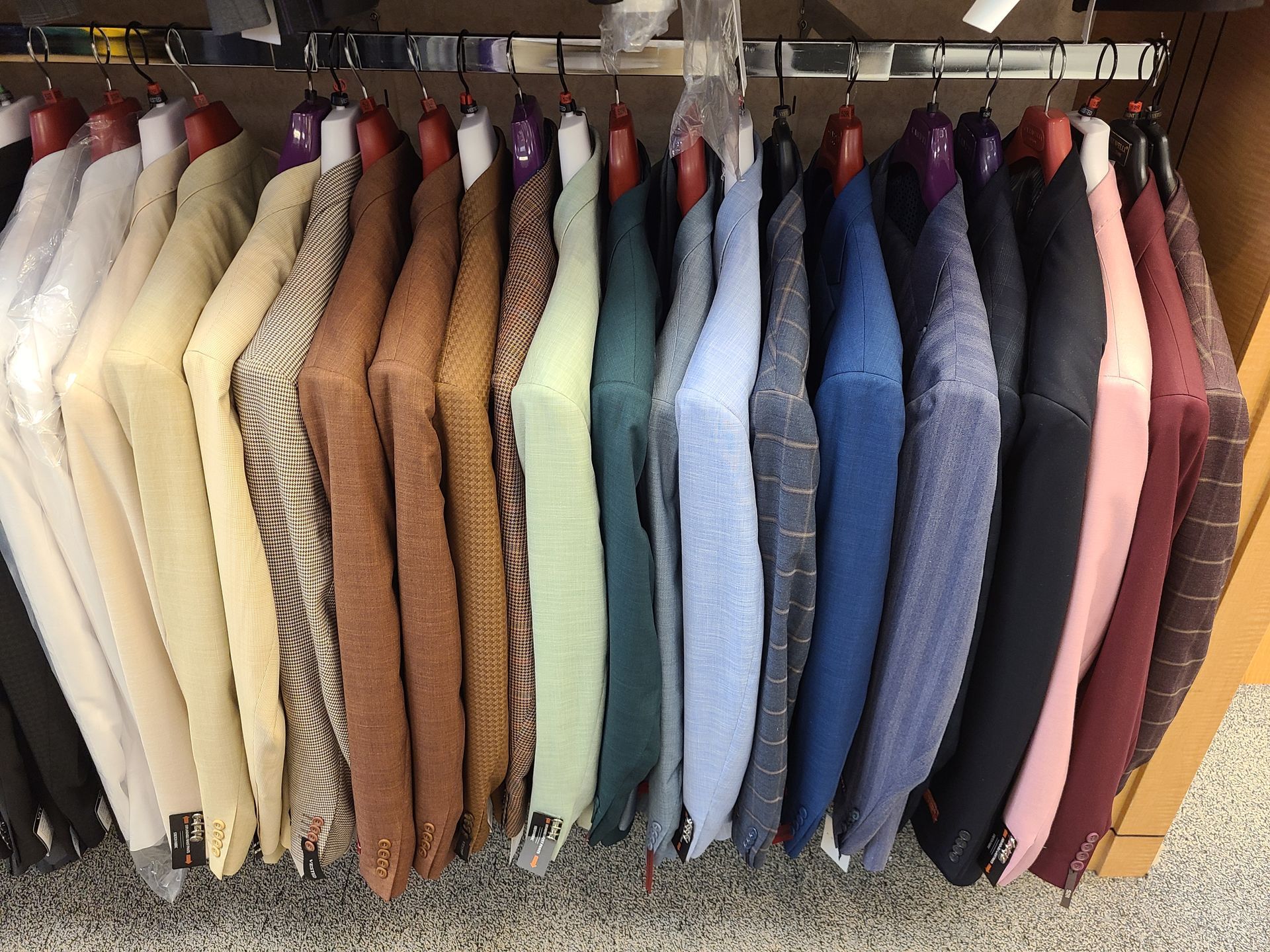Row of hanging sweaters and cardigans in cream, tan, blue, pink, and orange on a clothing rack