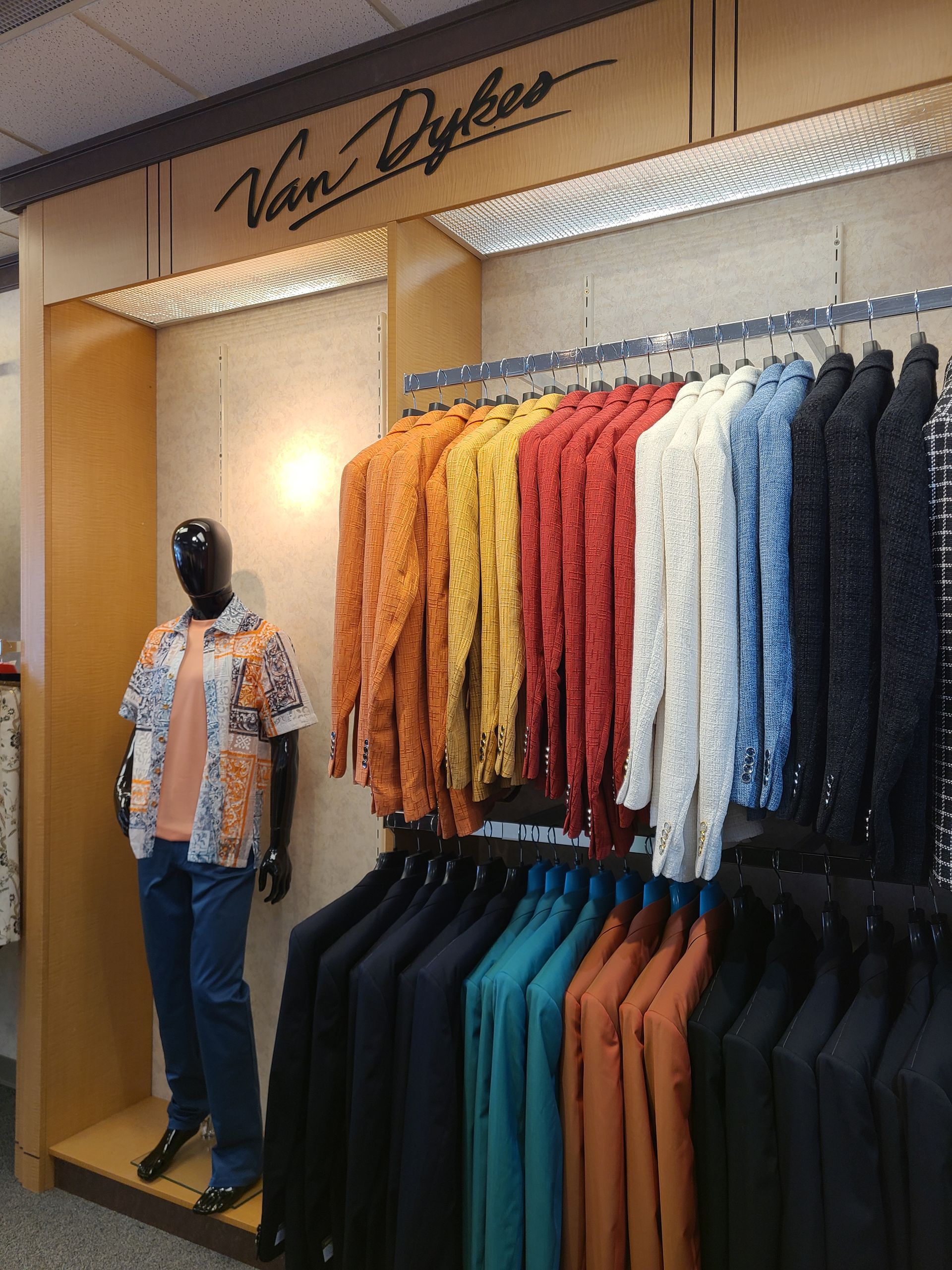 Clothing store display with a mannequin and racks of colorful shirts, jackets, and pants