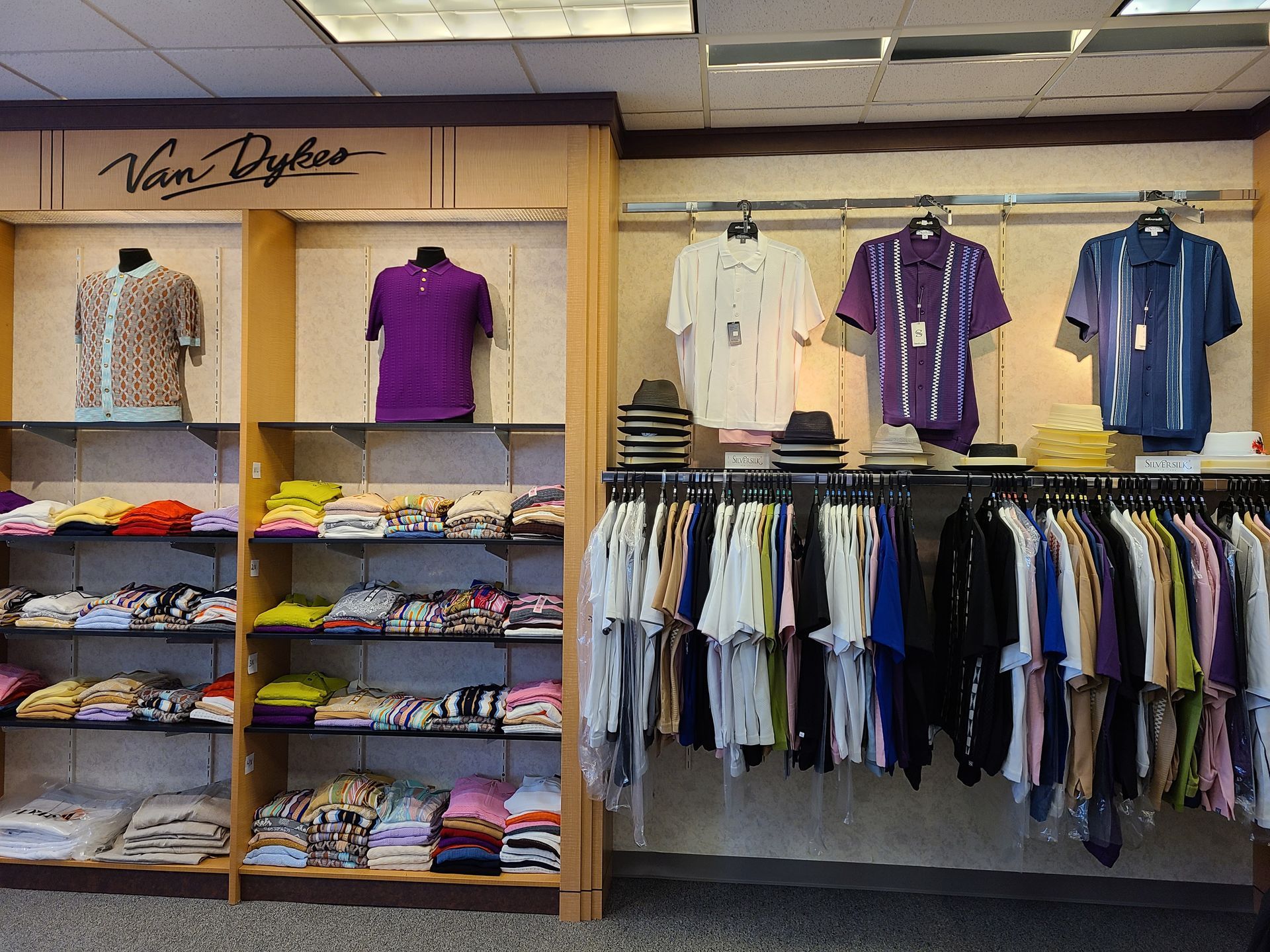 Clothing store display with folded shirts, hanging tops, and sweaters in a wooden retail rack.