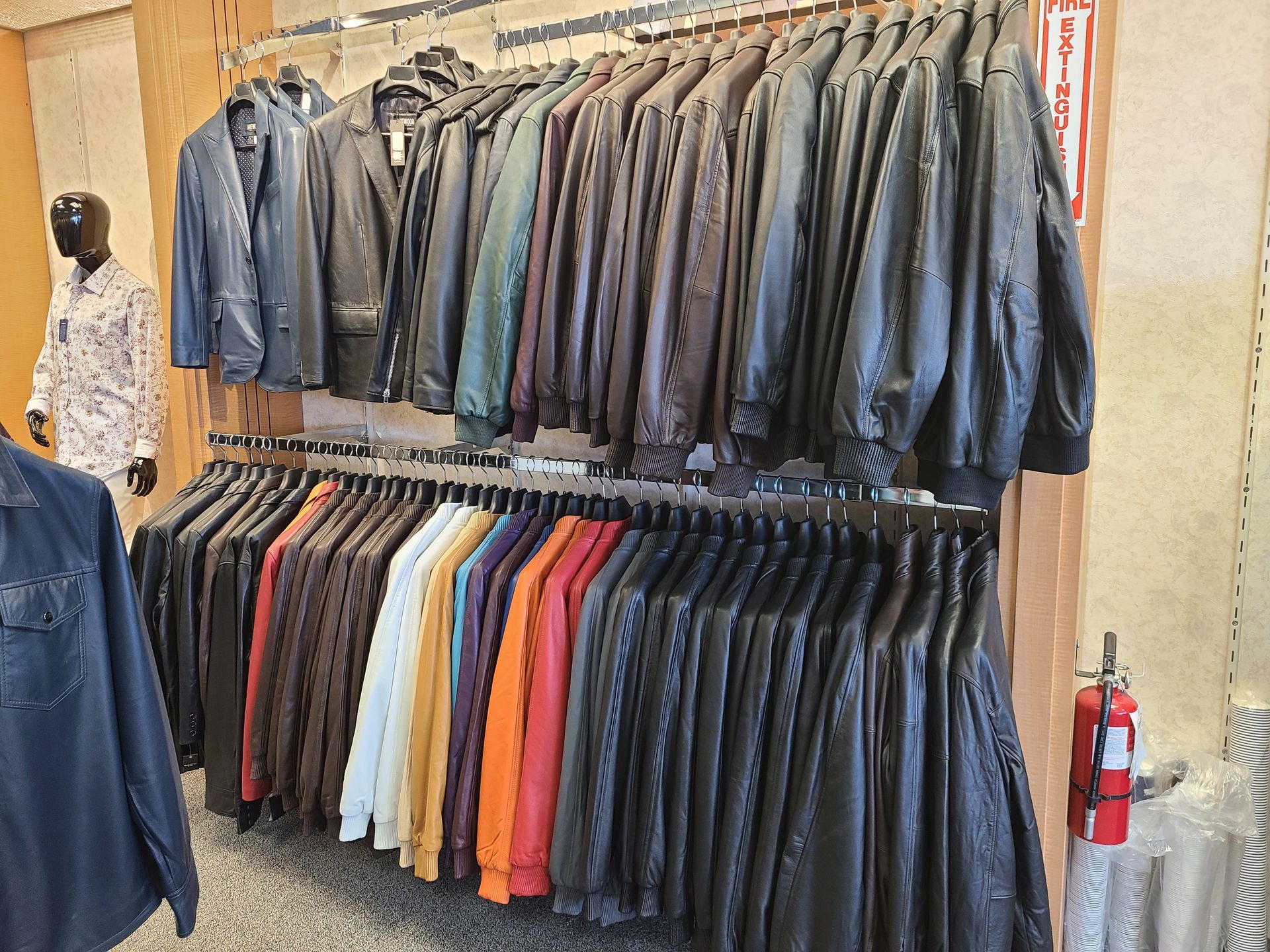 Jackets hang on racks in a store, mostly dark colors with some bright orange and red pieces.