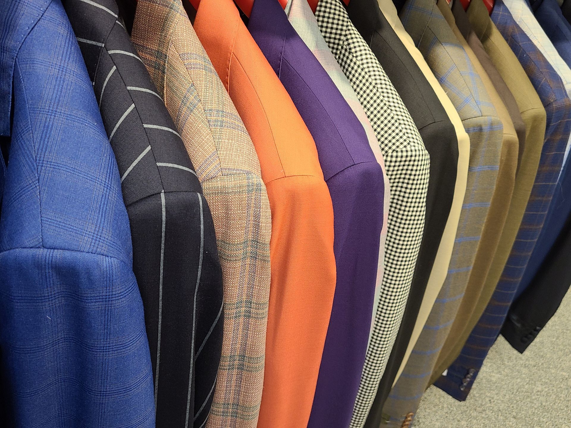 Colorful folded shirts on hangers in a clothing rack, including blue, black, orange, purple, and tan fabrics
