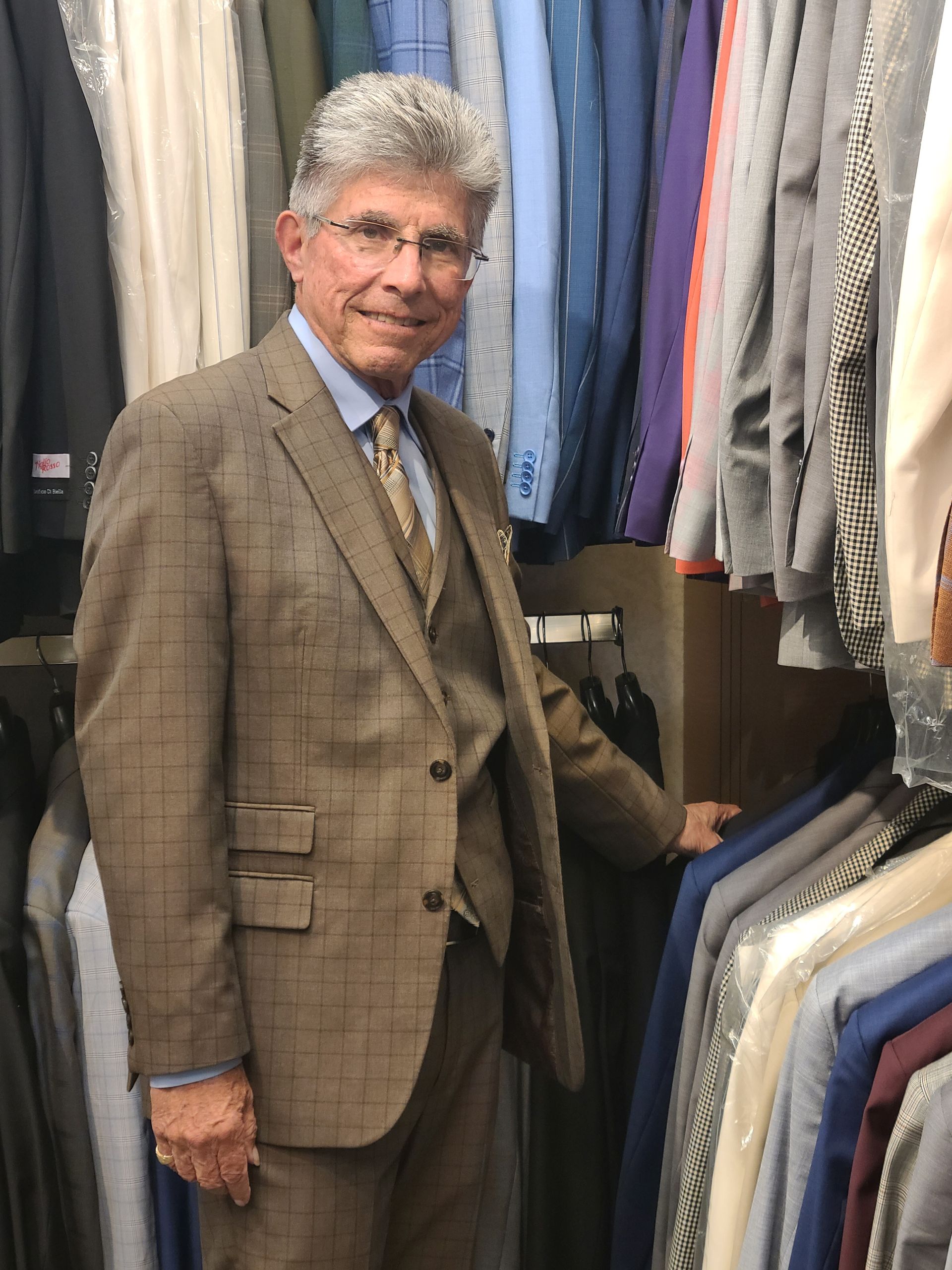Man in a brown suit standing in a clothing store aisle between rows of hanging garments