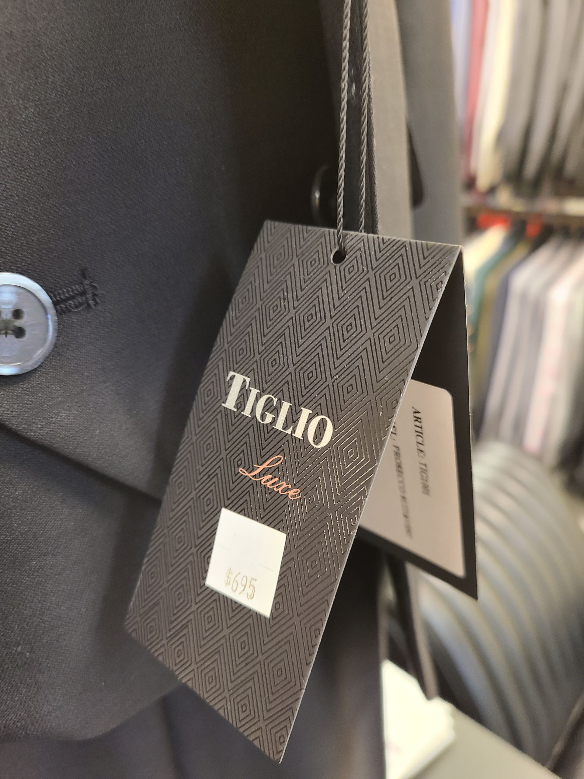 Black textured clothing tag with silver lettering and a small white label hanging from a black bag.