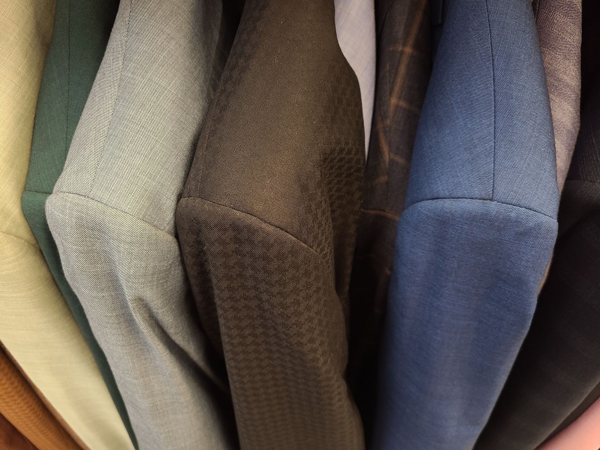 Close-up of hanging textured jackets in beige, brown, blue, and black.