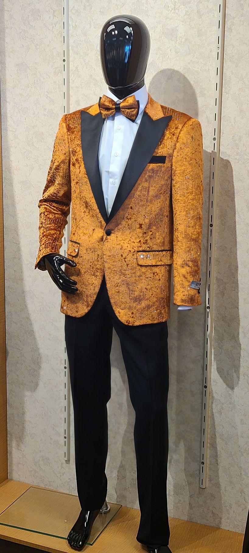 Mannequin in orange patterned tuxedo jacket with black lapels, bow tie, and black trousers in a showroom.