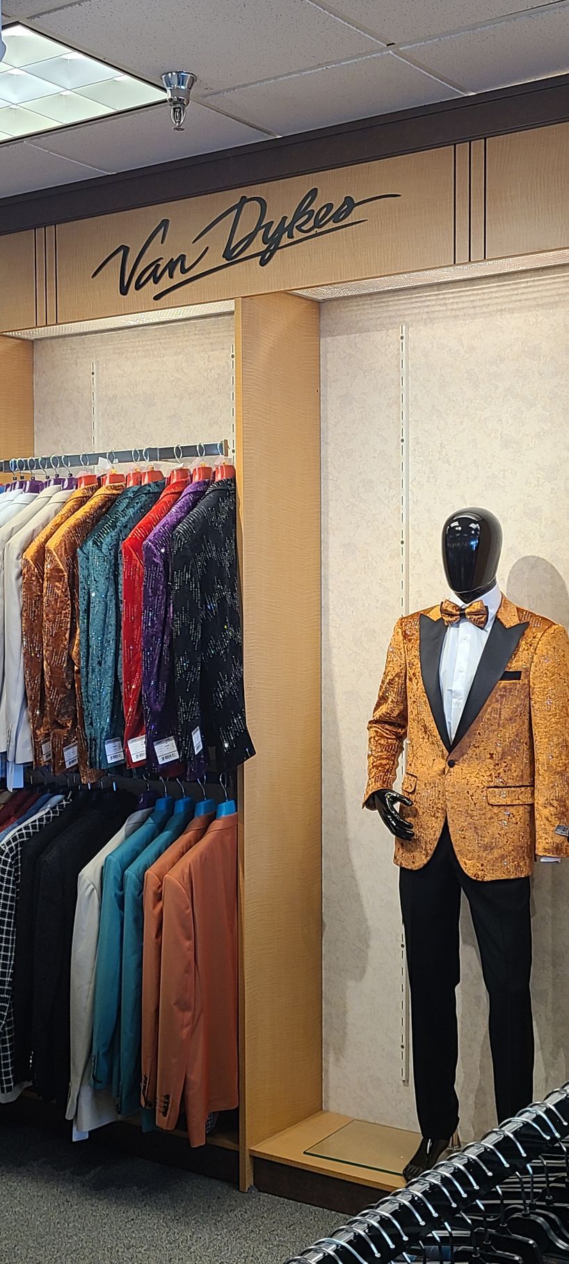 Boutique clothing display with colorful shirts, tan coats, and a mannequin in a gold jacket and bow tie.