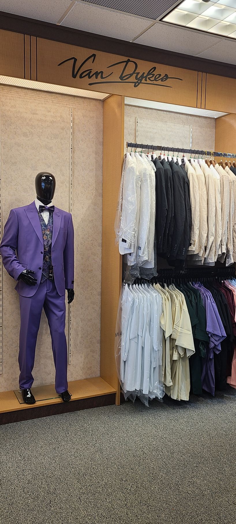 Men’s suit display with a purple suit on a mannequin beside racks of shirts and jackets.