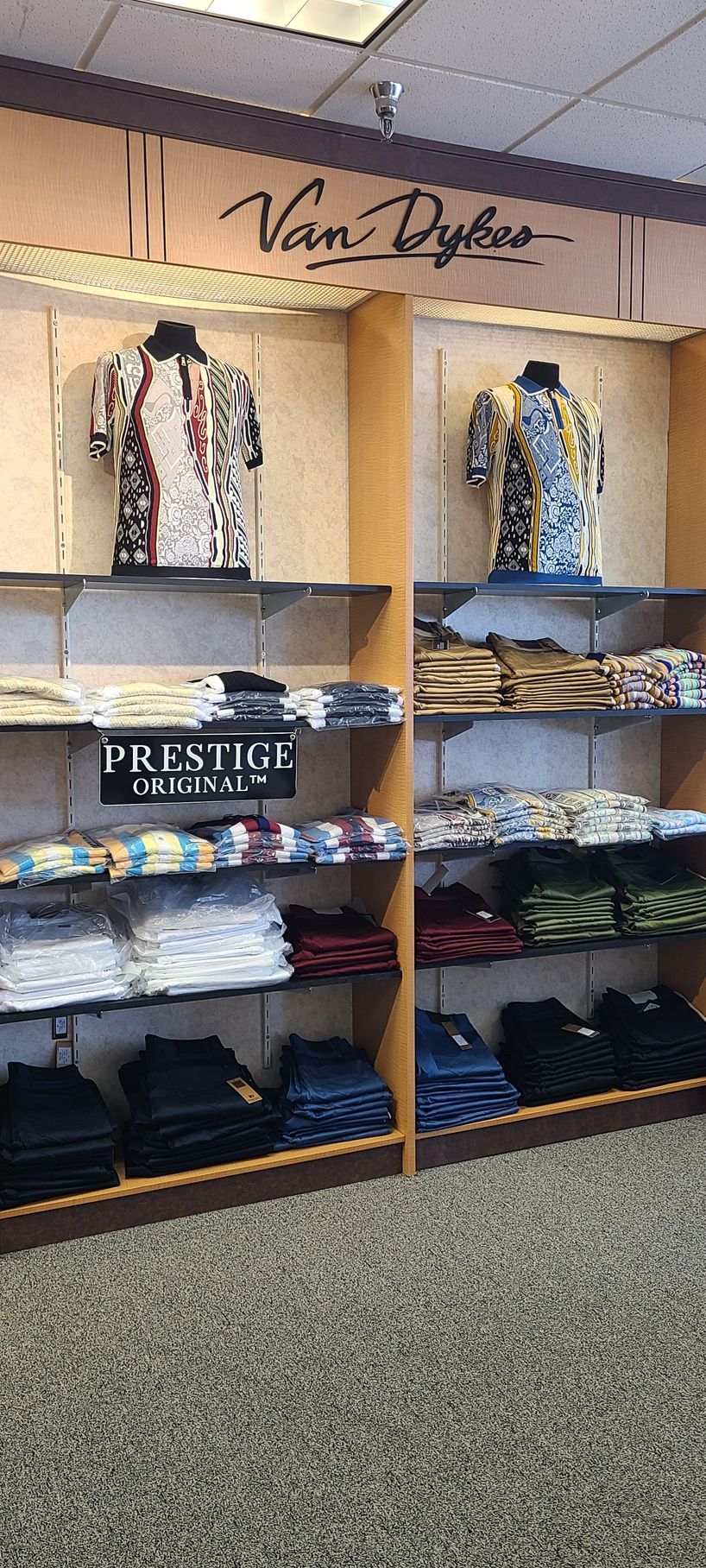 Clothing display with folded jeans and shirts on shelves under hanging patterned tops in a store.