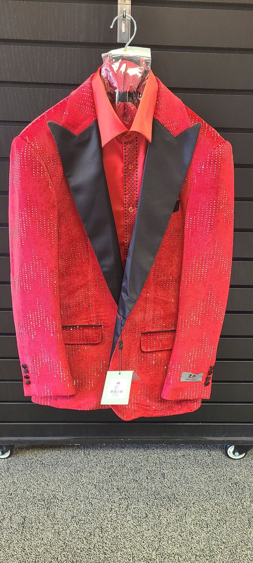 Red sequined tuxedo jacket with black lapels hanging on a rack against a dark wall.