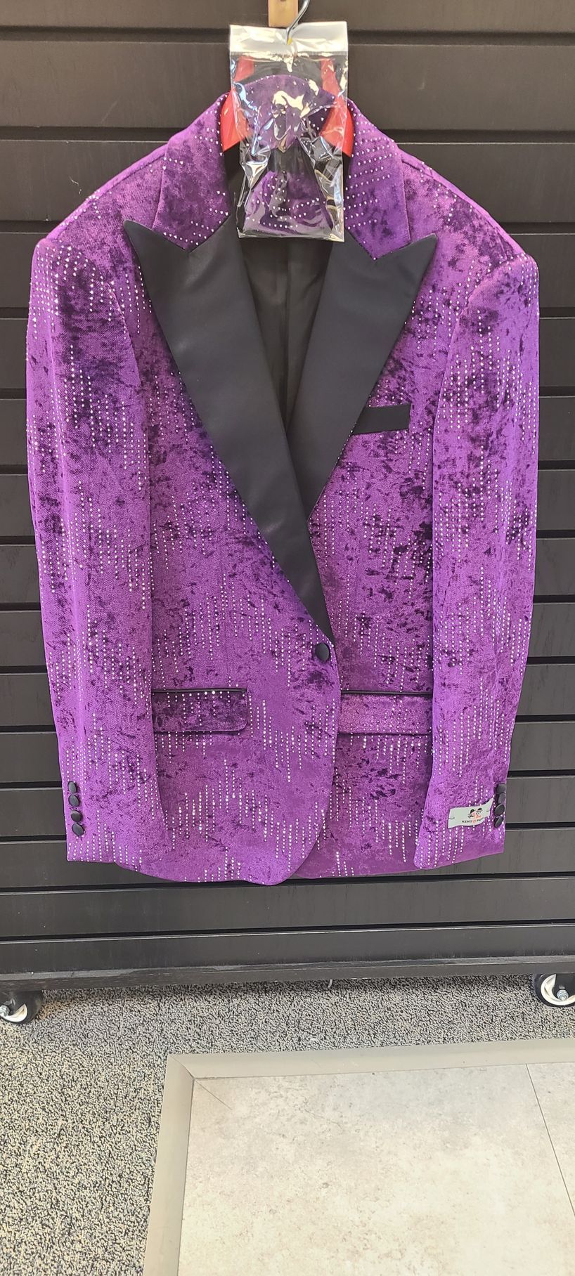 Purple sequined tuxedo jacket on a hanger against a dark wall