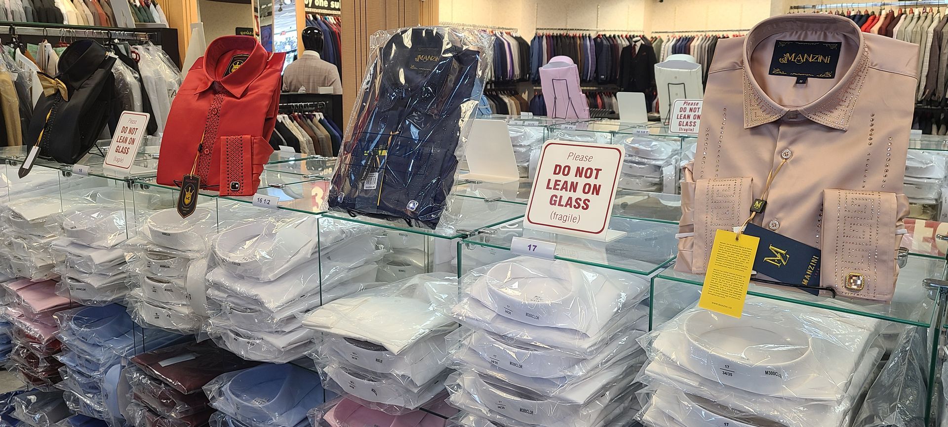 Folded shirts and jackets displayed on a market stall with price tags and a handwritten sign