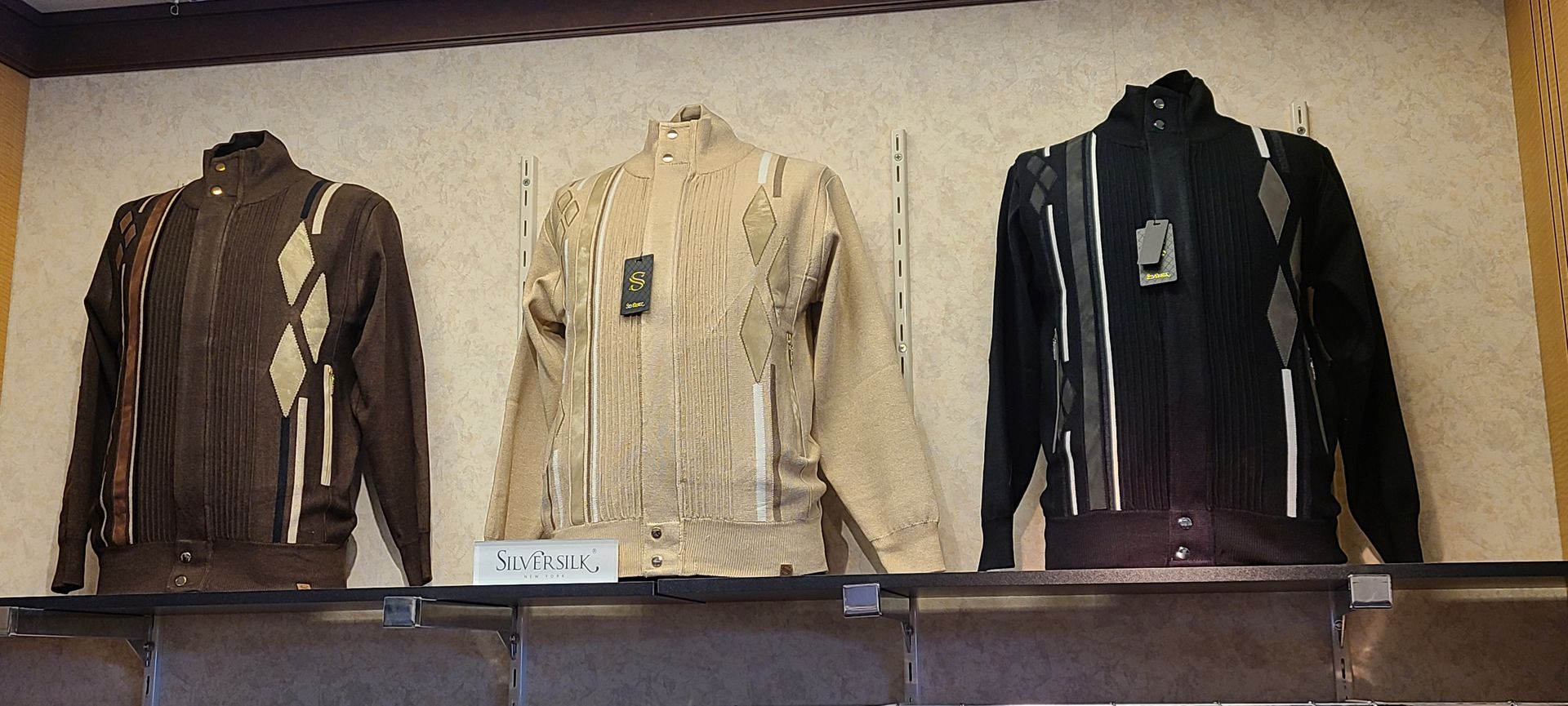 Three quilted jackets are on display in brown, beige, and black on a store shelf