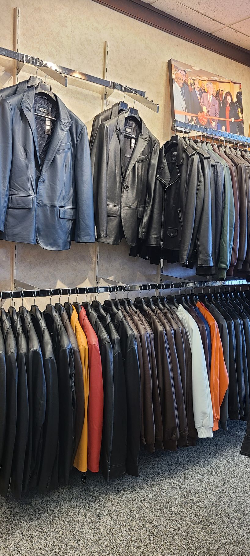 Clothing store display with rows of jackets and pants hanging on wall racks.