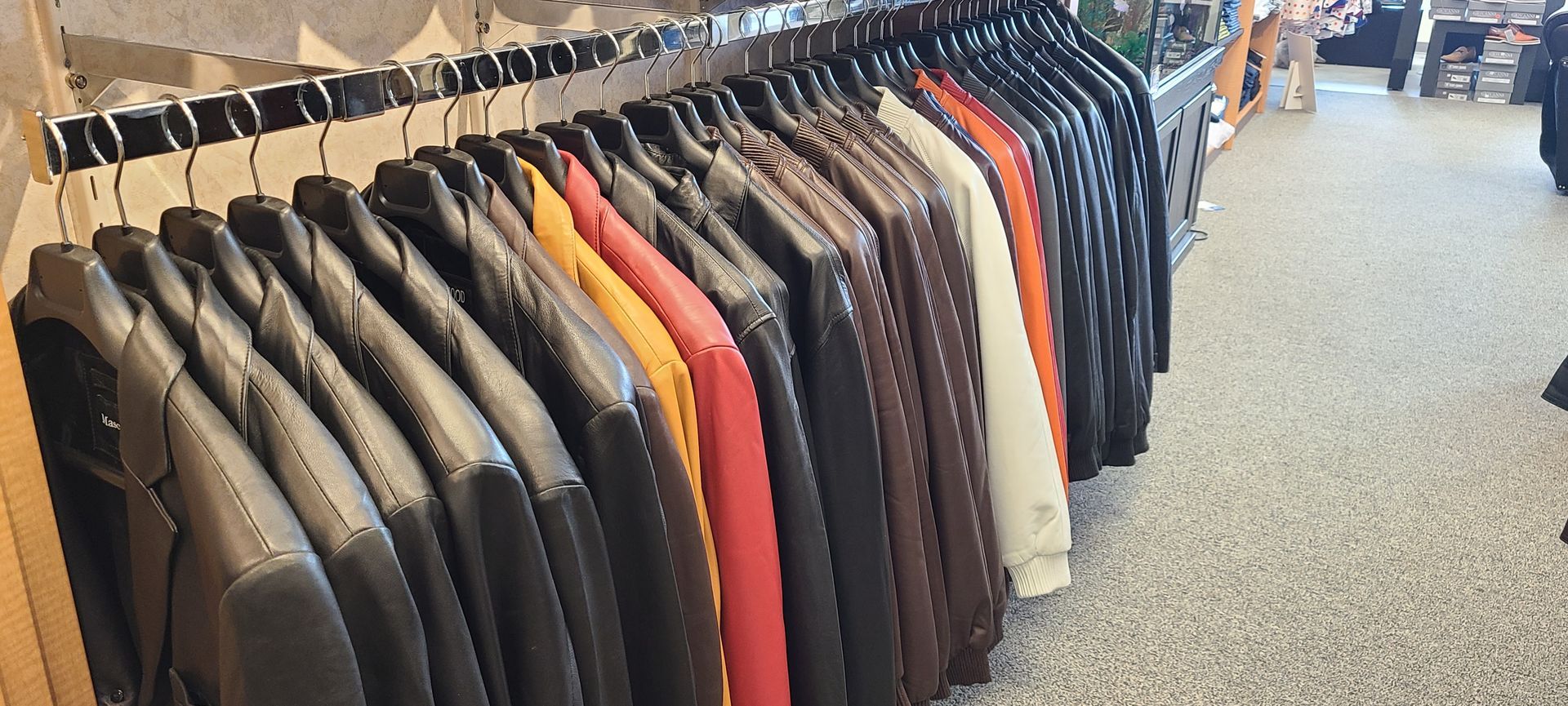 Racks of neatly hung jackets and blazers in a store aisle, with black, gray, tan, and a few orange pieces.