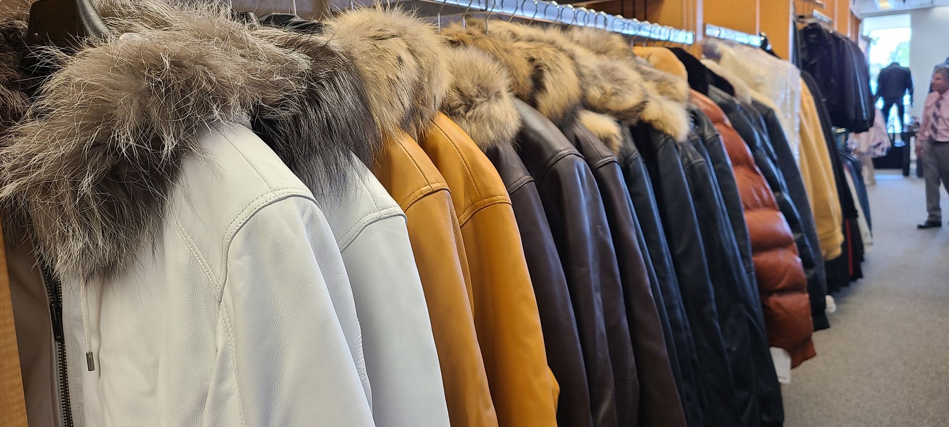 Racks of winter coats in neutral colors lined up in a clothing store aisle